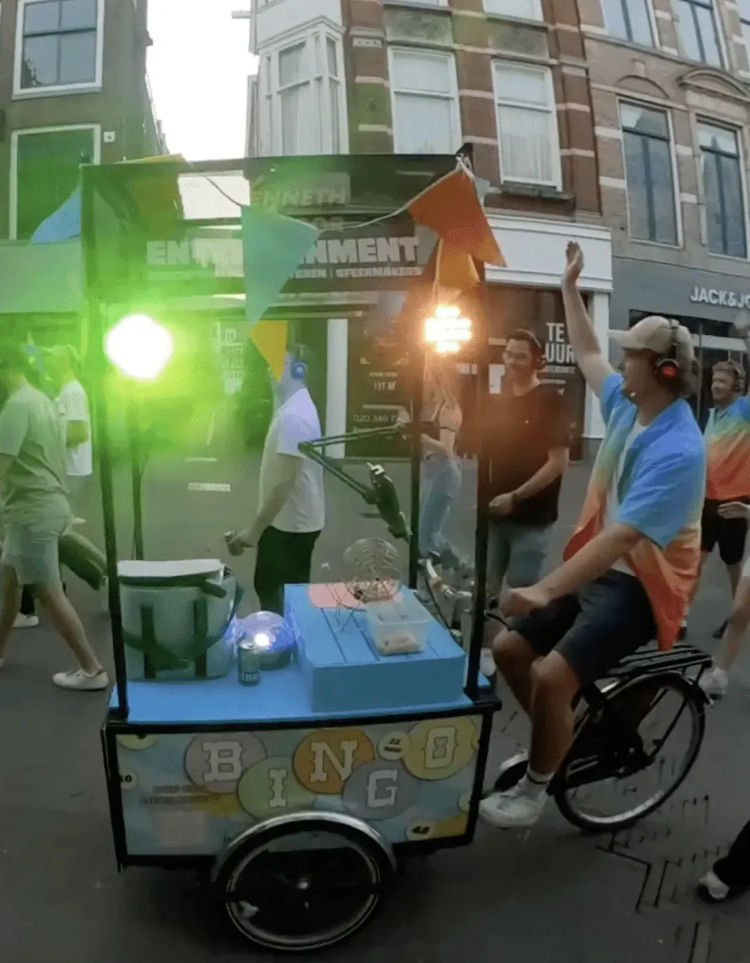 De Bingobakfiets rijdt met lichten aan door een straat met publiek