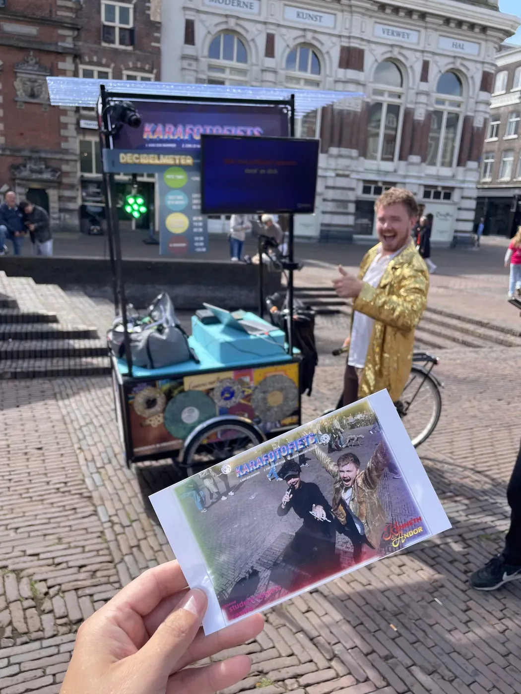 Hand houdt de zojuist geprinte foto omhoog met de Karafotofiets op de achtergrond