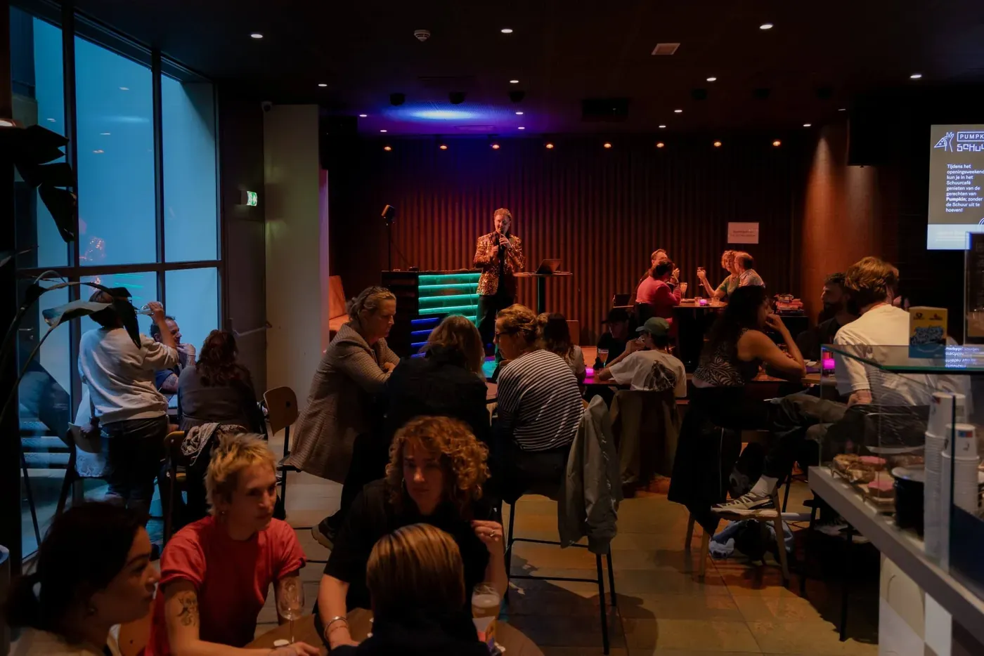 Volle zaal met teams aan tafels tijdens de Pubquiz Show, quizmaster op het podium