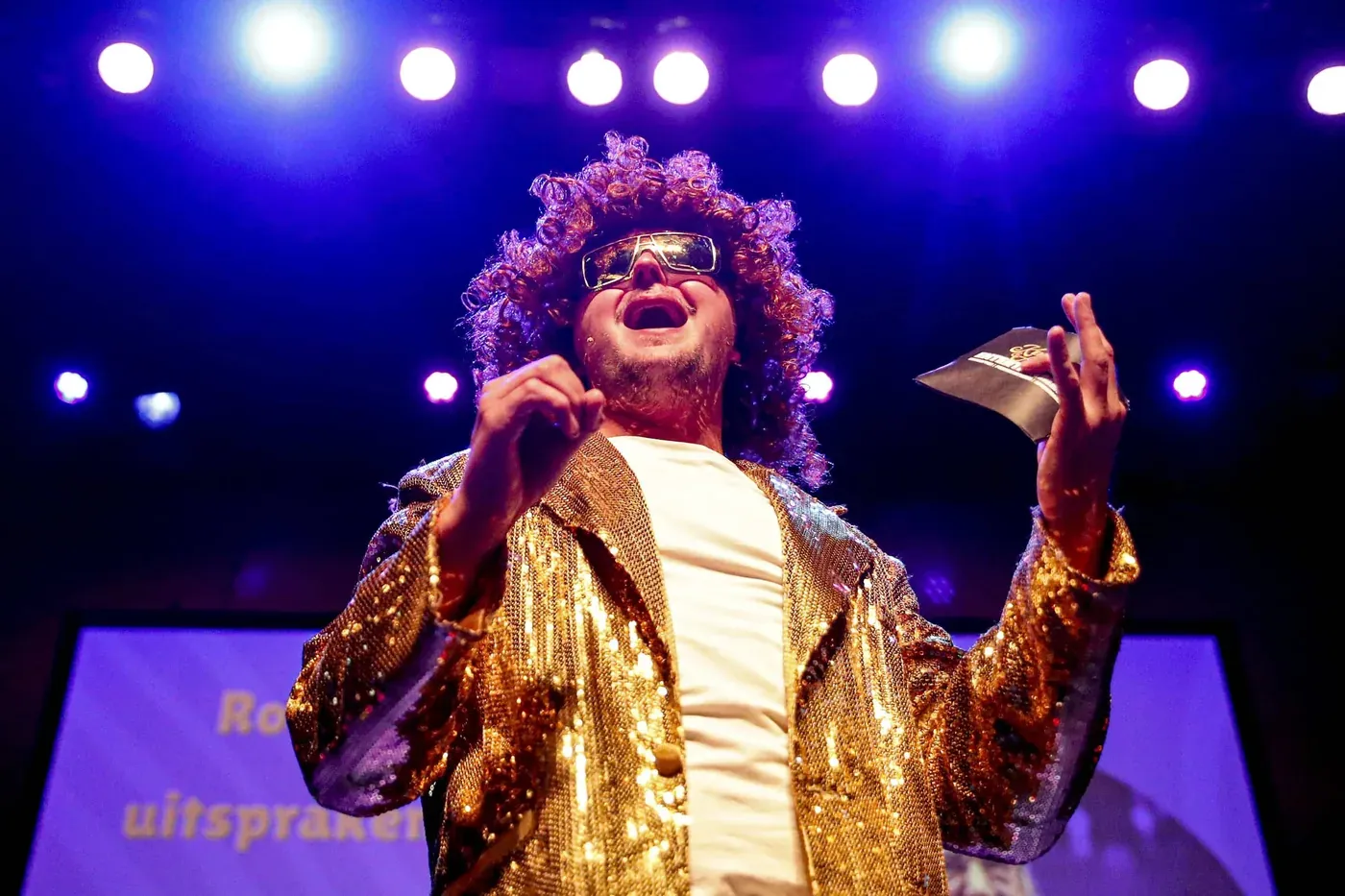 Showmaster in gouden pak zingt voor een volle zaal